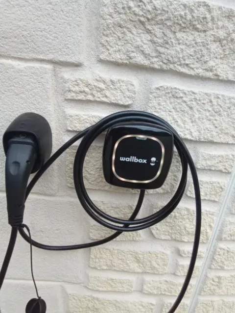 Borne de recharge murale noire avec son câble Type 2 lové, installée par Sanou Électricité